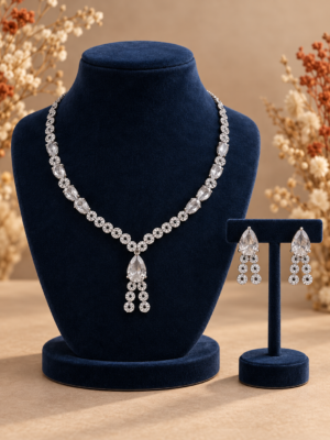 Riddhima white American diamond necklace with teardrop stones and floral detailing on a navy velvet bust, beside matching drop earrings