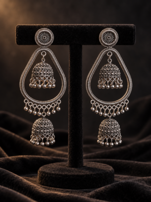 Pair of oxidised silver-tone earrings with open teardrop frames, two patterned jhumkas and dangling beads on a black velvet stand