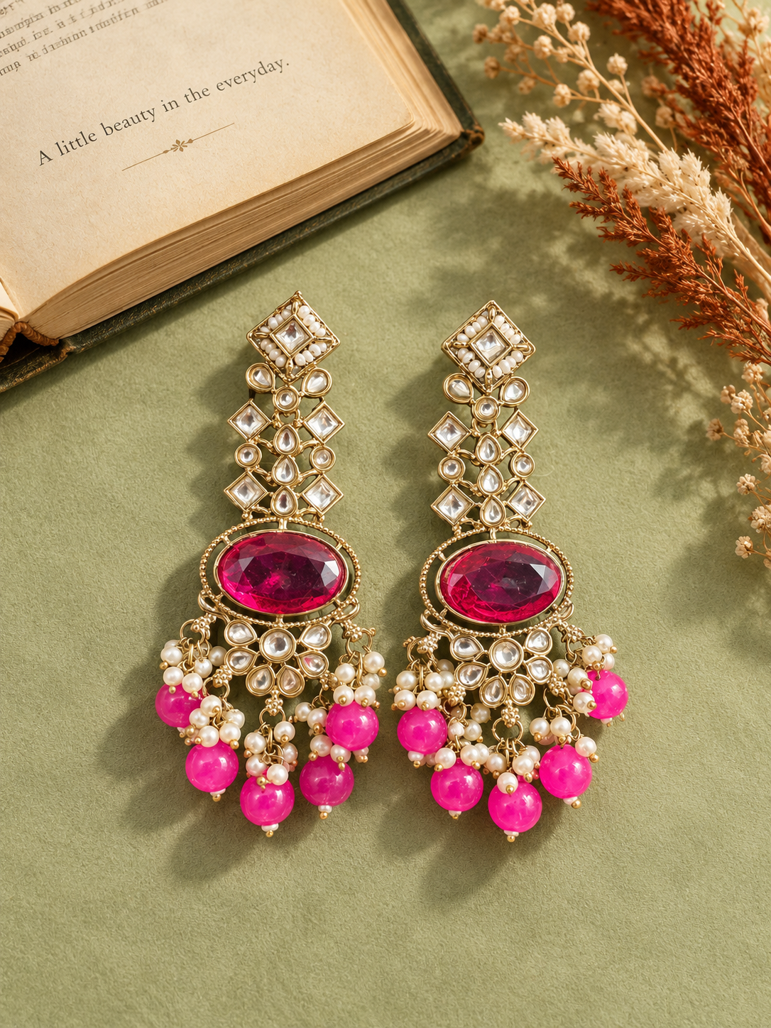 Saanvika dark pink Kundan dangler earrings with oval pink centres and bead drops on a sage green surface