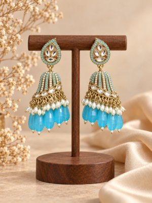 Chitra light blue jhumka earrings with gold-tone domes, white bead accents and elongated blue drops, held in a hand